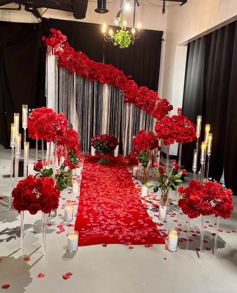 Red rose proposal aisle with candlelit walkway and cascading floral backdrop inside a modern event studio.